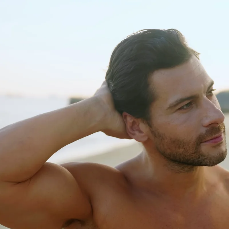 Model running a hand through styled hair on a beach at golden hour